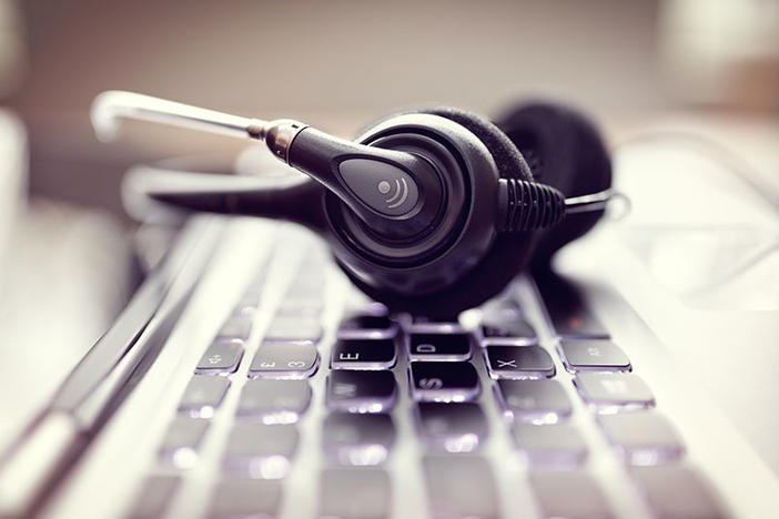 Picture of a computer keyboard and headphones with a microphone attachment.